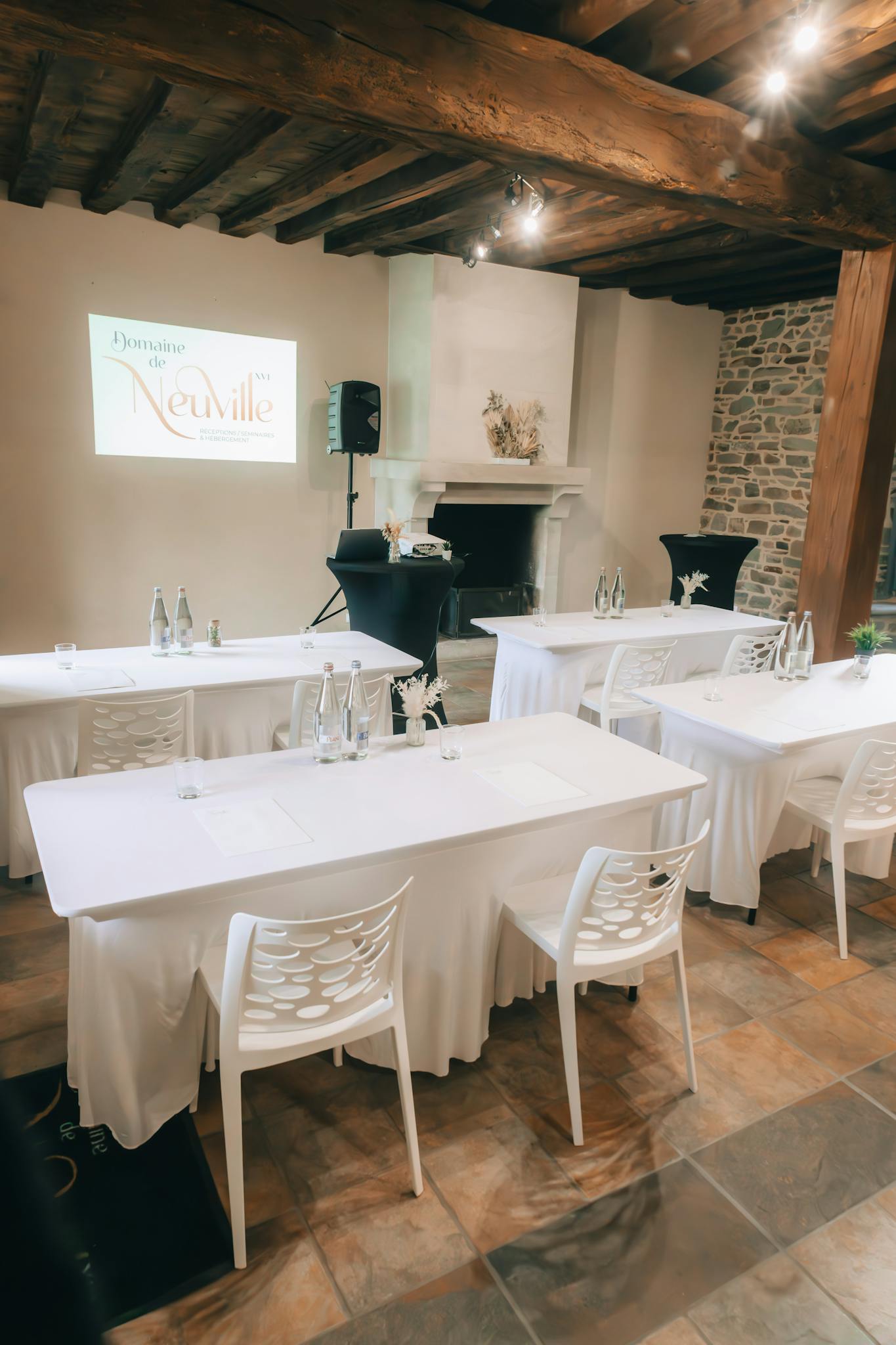 A neat banquet hall setup with white tablecloths and chairs in a rustic indoor venue.